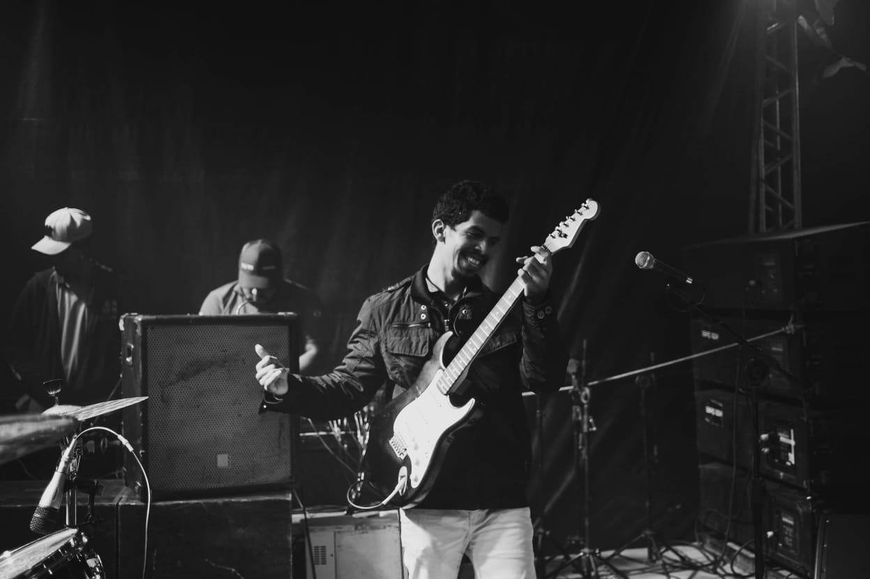 Edésio César sorrindo e tocando guitarra em uma apresentação ao vivo
